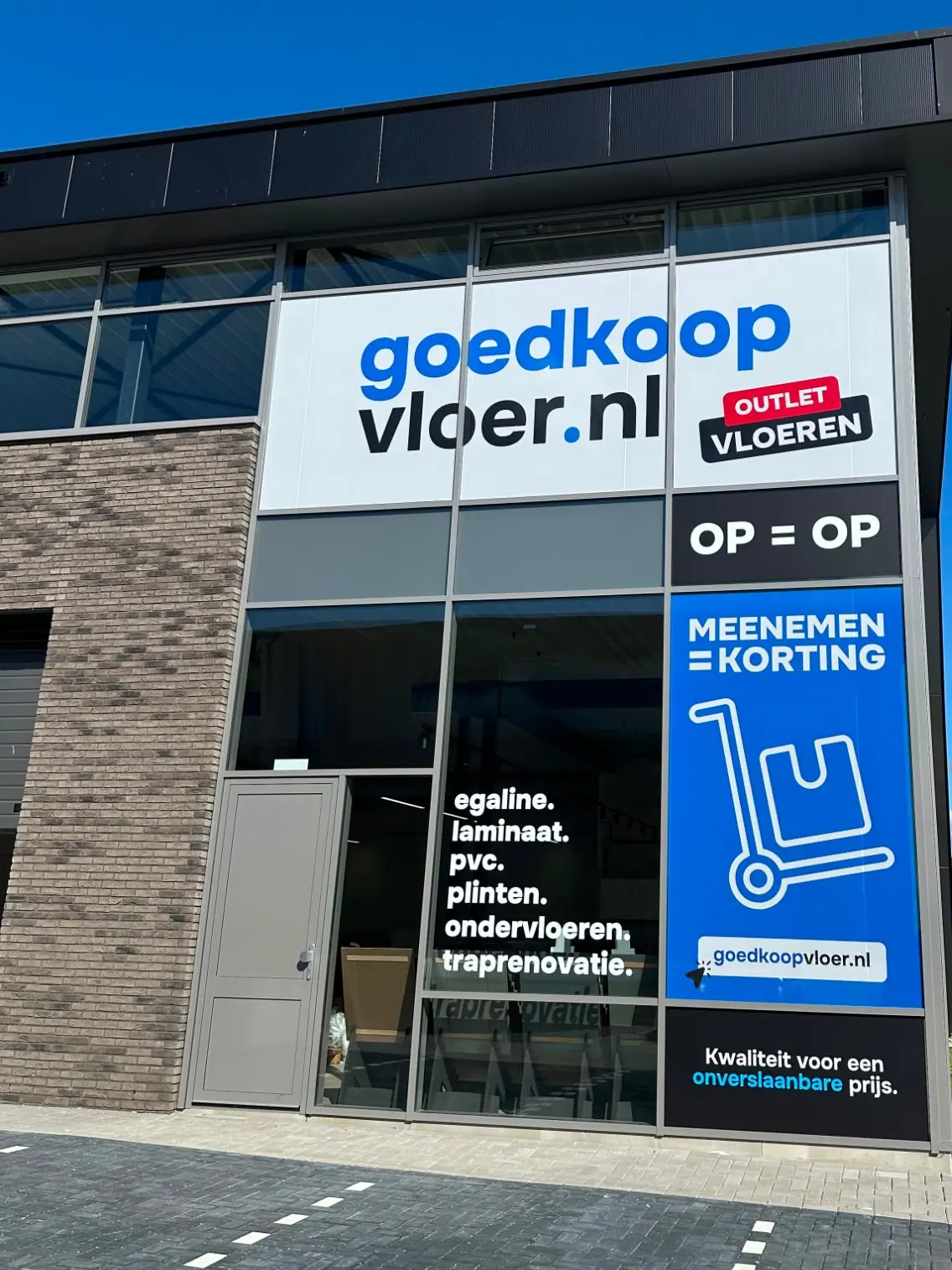Voorgevel van de winkel met het logo bovenaan, een blauw raamvlak met een steekwagen en de productgroepen op het raam