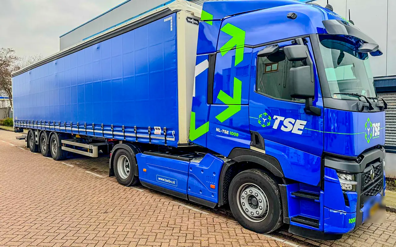 Blauwe trekker van TSE met groene pijlen op de cabine en het TSE-logo op de deur, met een blauwe oplegger met schuifzeil
