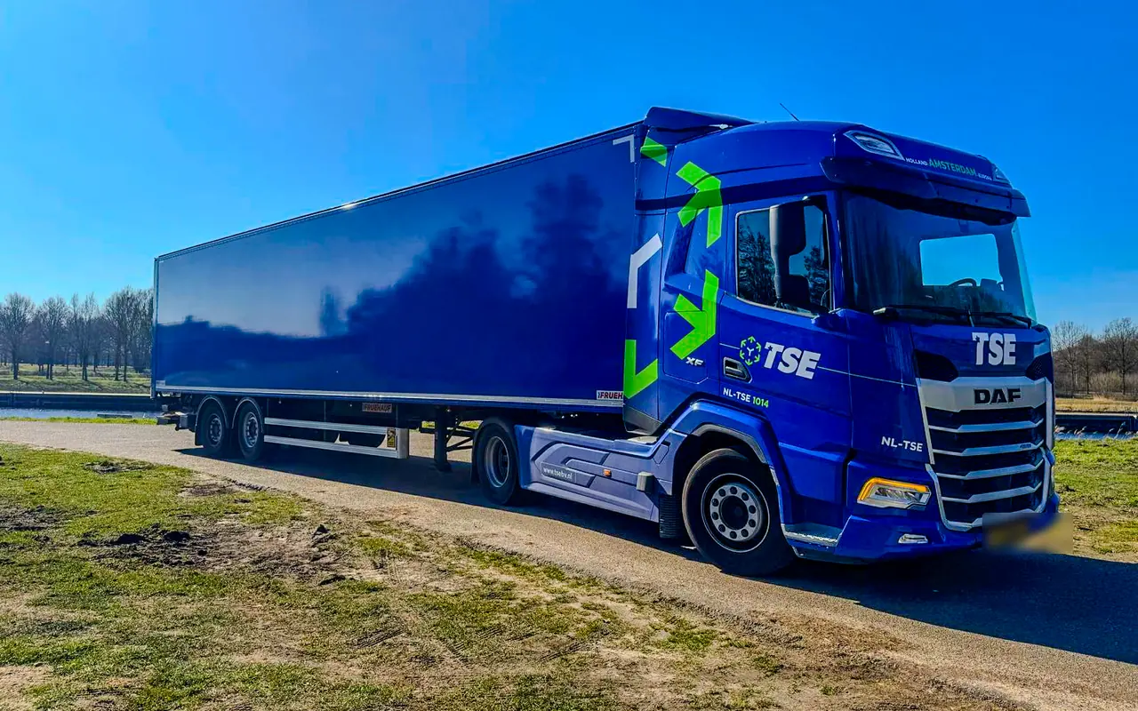 Trekker van TSE met groene pijlen en het logo op de cabine, met een blauwe gesloten oplegger